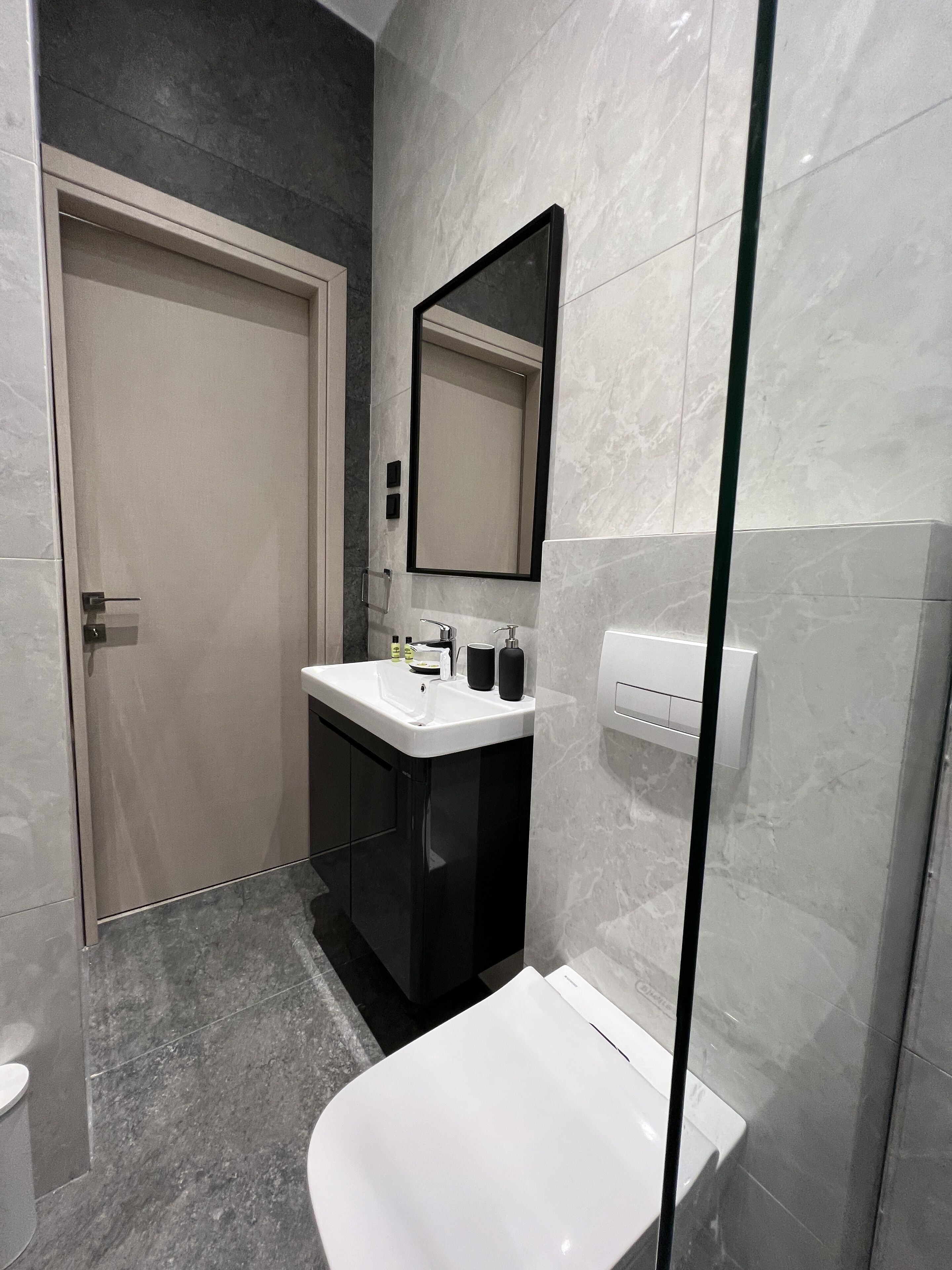 A modern bathroom with a white sink, black cabinet, and a large mirror.