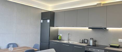 Una cocina moderna con armarios grises, horno empotrado y una zona de comedor con sofá gris y mesa de madera.