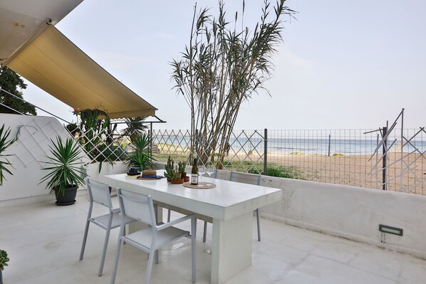 A patio with a white table and chairs, potted plants, and a view of the beach.