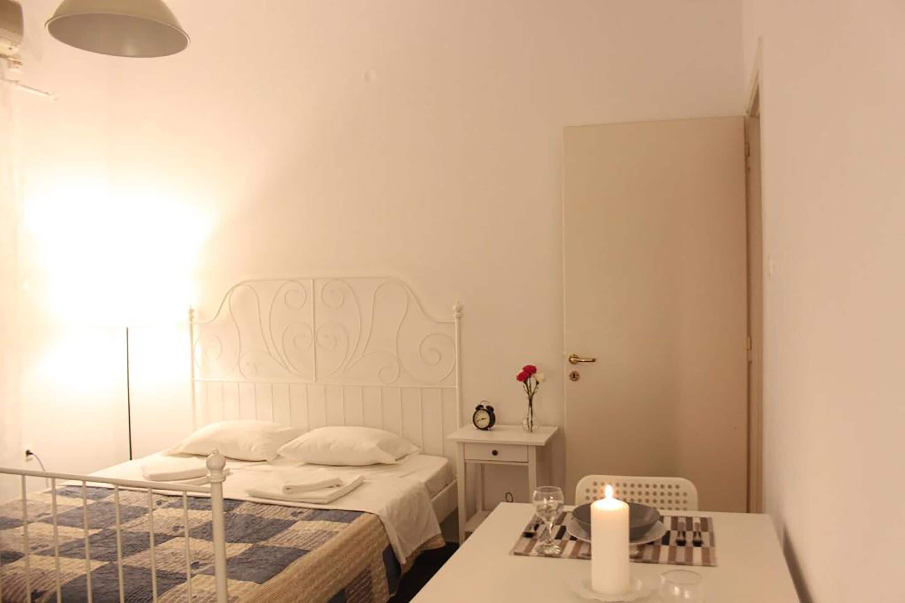 Een keurig opgemaakt slaapkamer met een bed, nachtkastje en een tafeltje met een kaars.