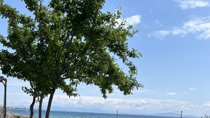 Un espace extérieur aménagé avec une table et des chaises, donnant sur une plage parsemée de parasols et offrant une vue sur la mer et les montagnes.