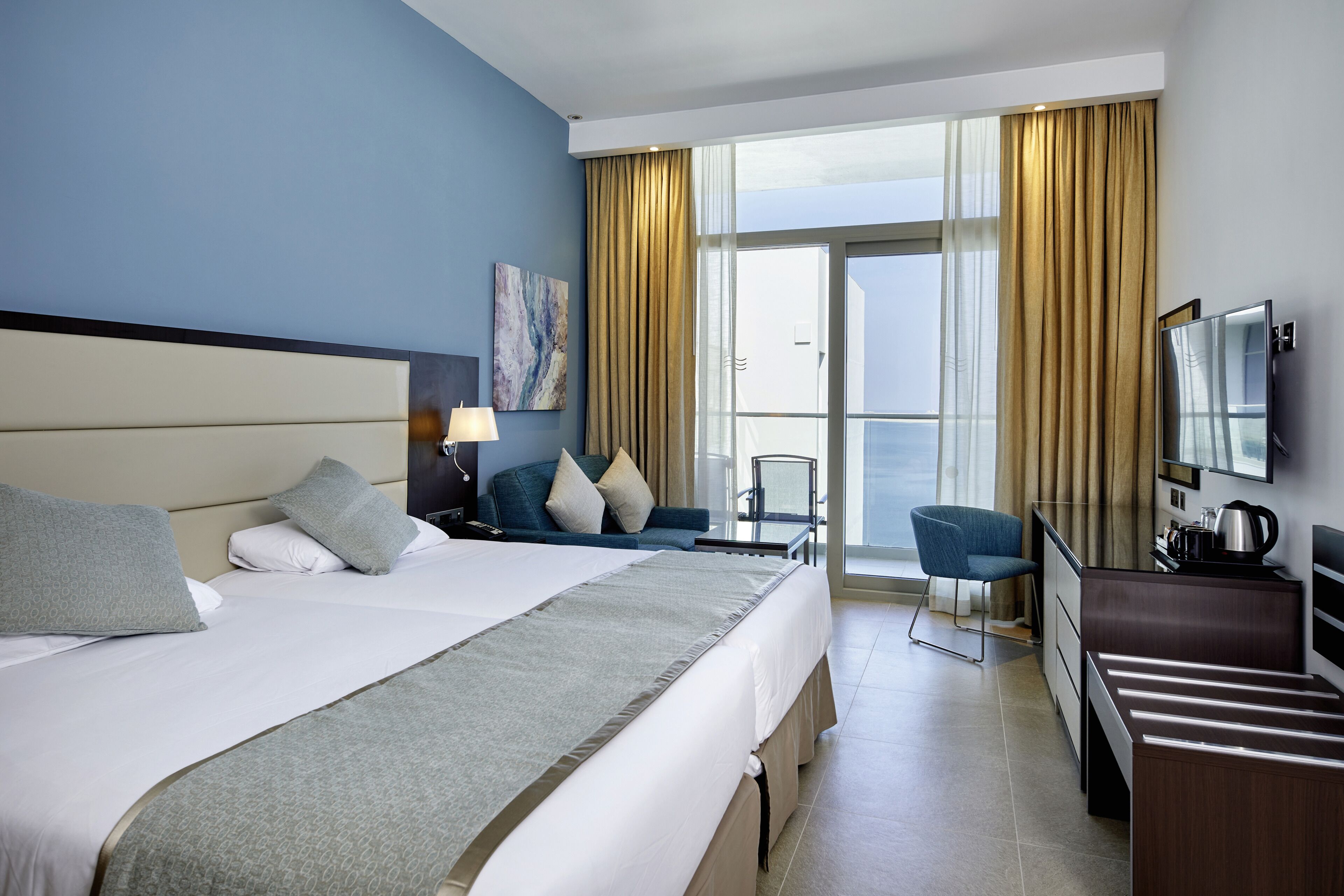 A hotel room with a large bed, a desk, a chair, a television, and a view of the outdoors.
