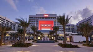 A hotel with a prominent 'RIU' sign, a central fountain, and a landscaped area with palm trees and lounge chairs.