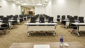 Un salón de conferencias con varias mesas, sillas y botellas de agua.