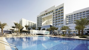 A modern hotel with a swimming pool, palm trees, and sun loungers.