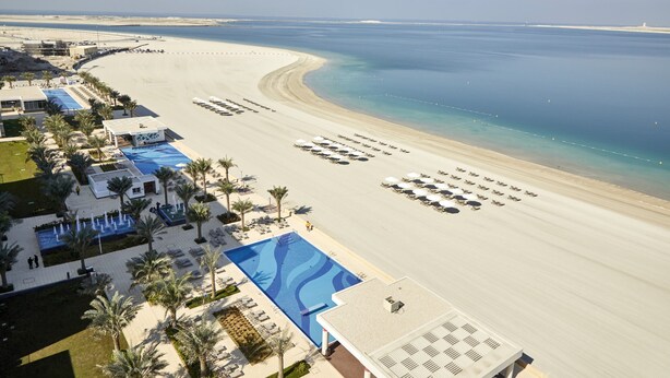 A resort with a large pool, beachside lounge chairs, and a view of the ocean.
