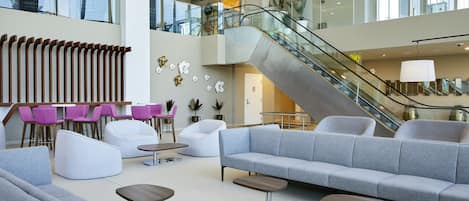 A spacious lobby with a central seating area, a staircase, and a view of the upper floor.