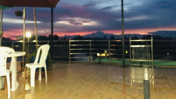 An outdoor seating area with a wooden deck, white plastic chairs, and a red umbrella. - Grand Star Guest House (Batticaloa)