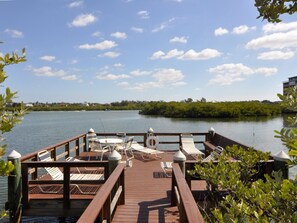 Um deck de madeira com cadeiras de lounge e uma mesa, com vista para um corpo d'água calmo e céu claro.