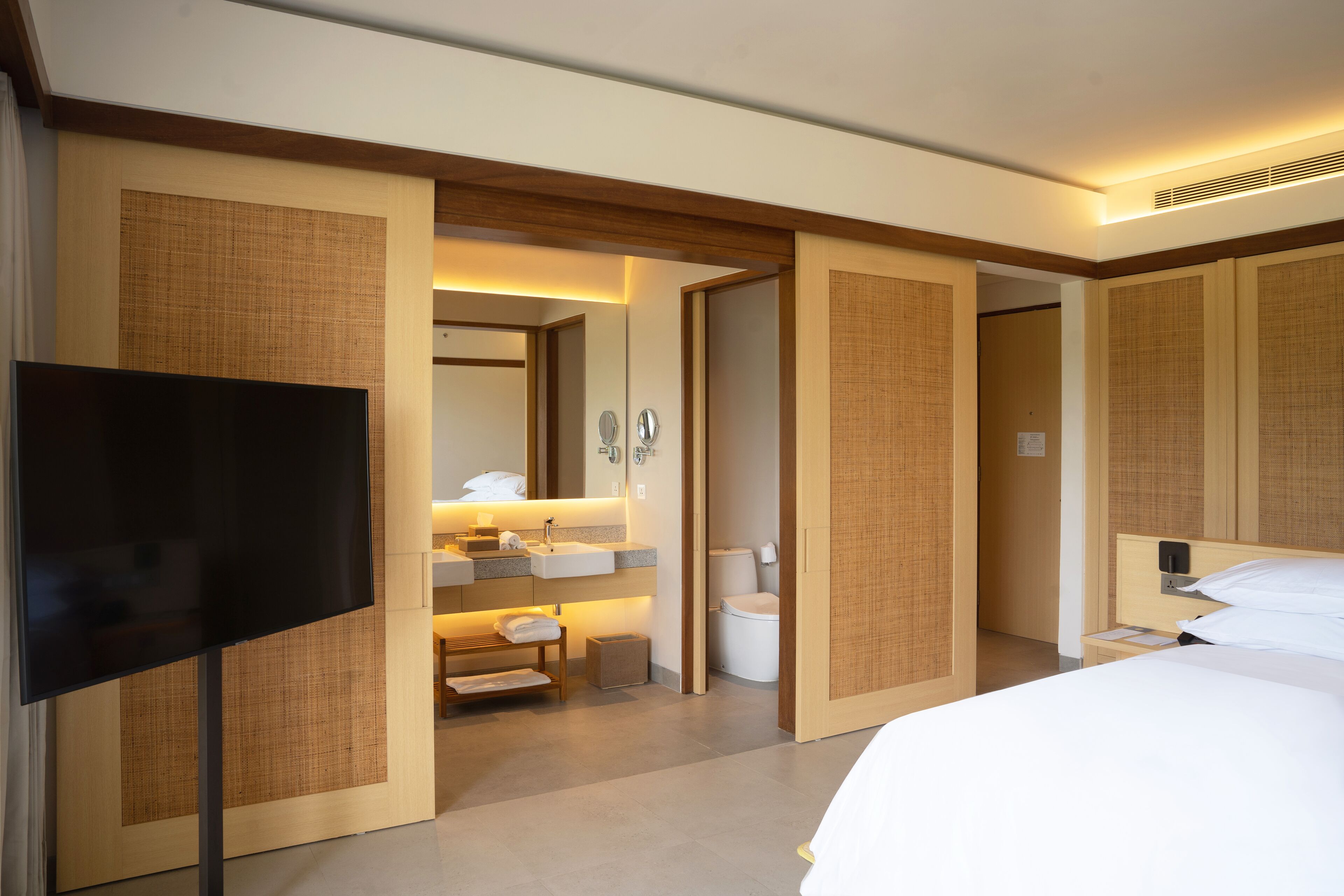 Quarto de hotel com uma cama, televisão, banheiro com pia e vaso sanitário, e um espelho.