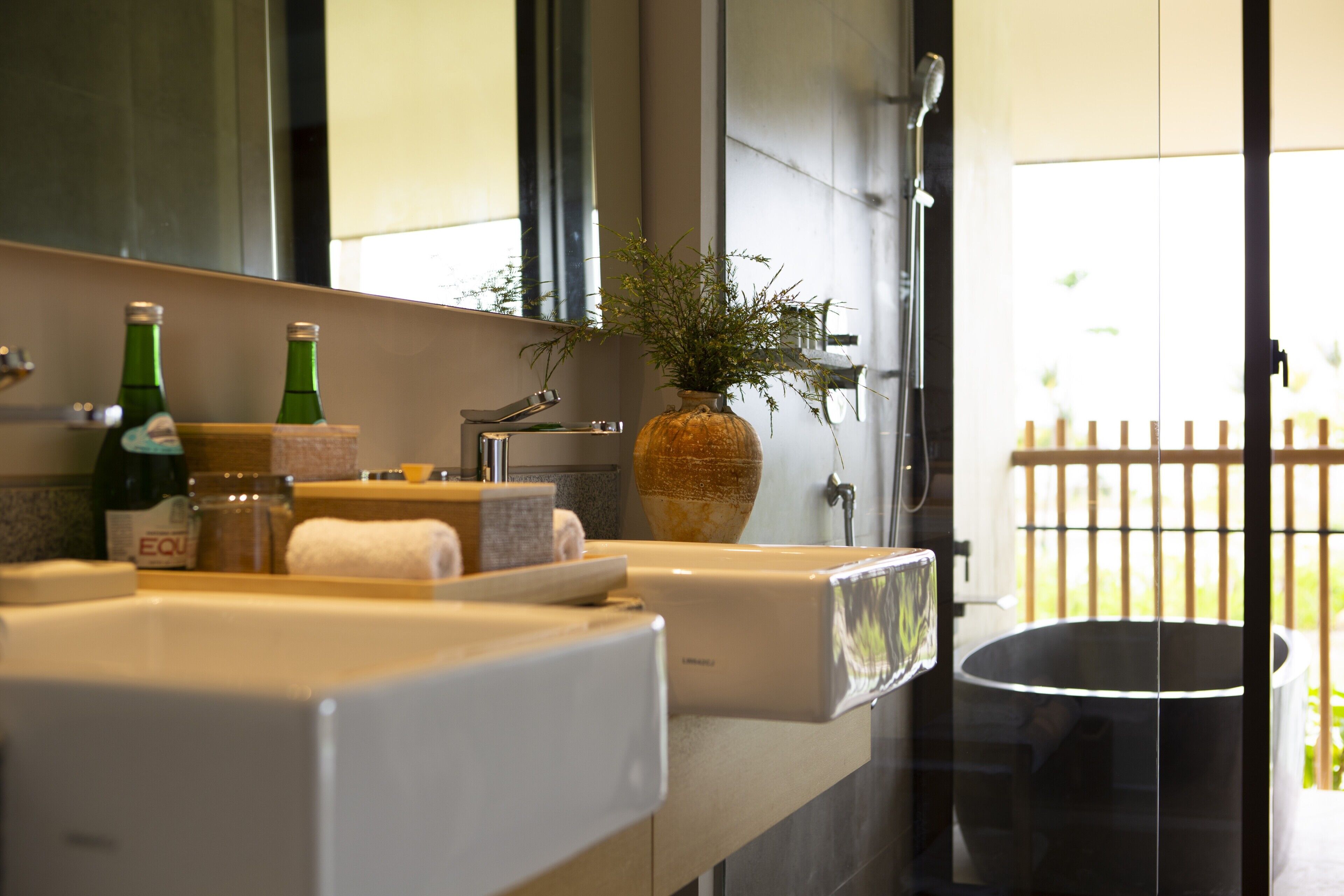 A bathroom with a large mirror, a sink, a vase with a plant, and a shower area.