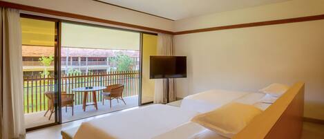 Habitación de hotel con una cama grande, televisión, balcón con mesa y sillas, y vista del edificio exterior.