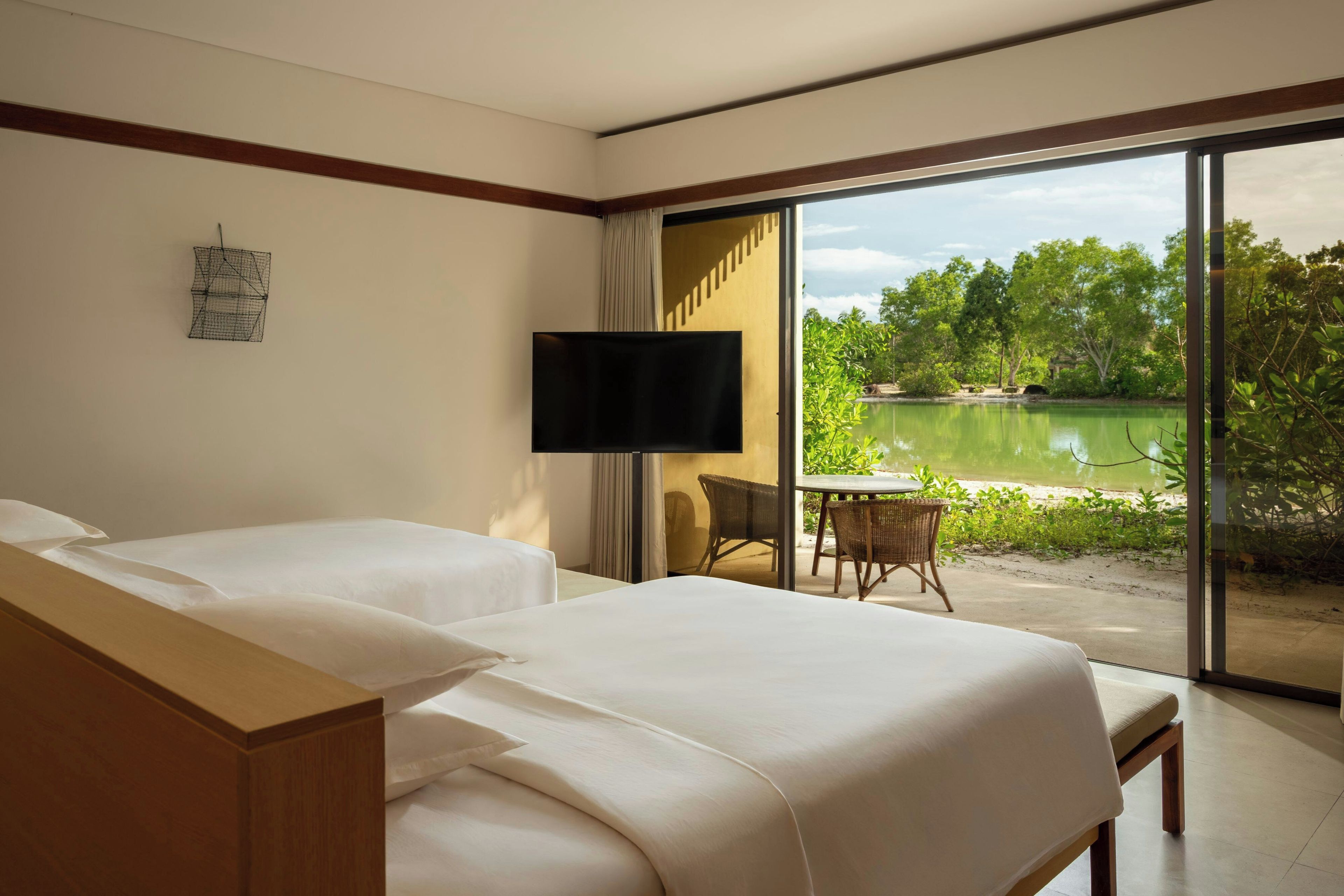 Habitación de hotel con dos camas, un televisor, una mesita con sillas y vista a un lago.