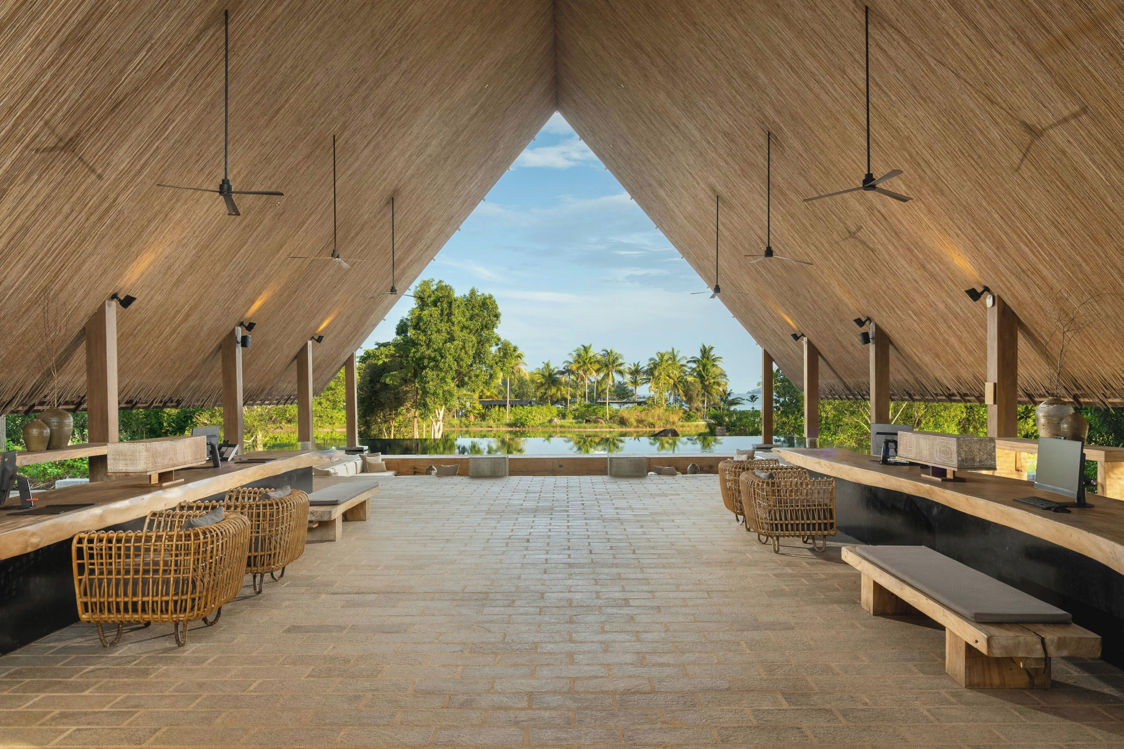 An outdoor seating area with tables and chairs, a brick floor, and a view of a body of water and trees.