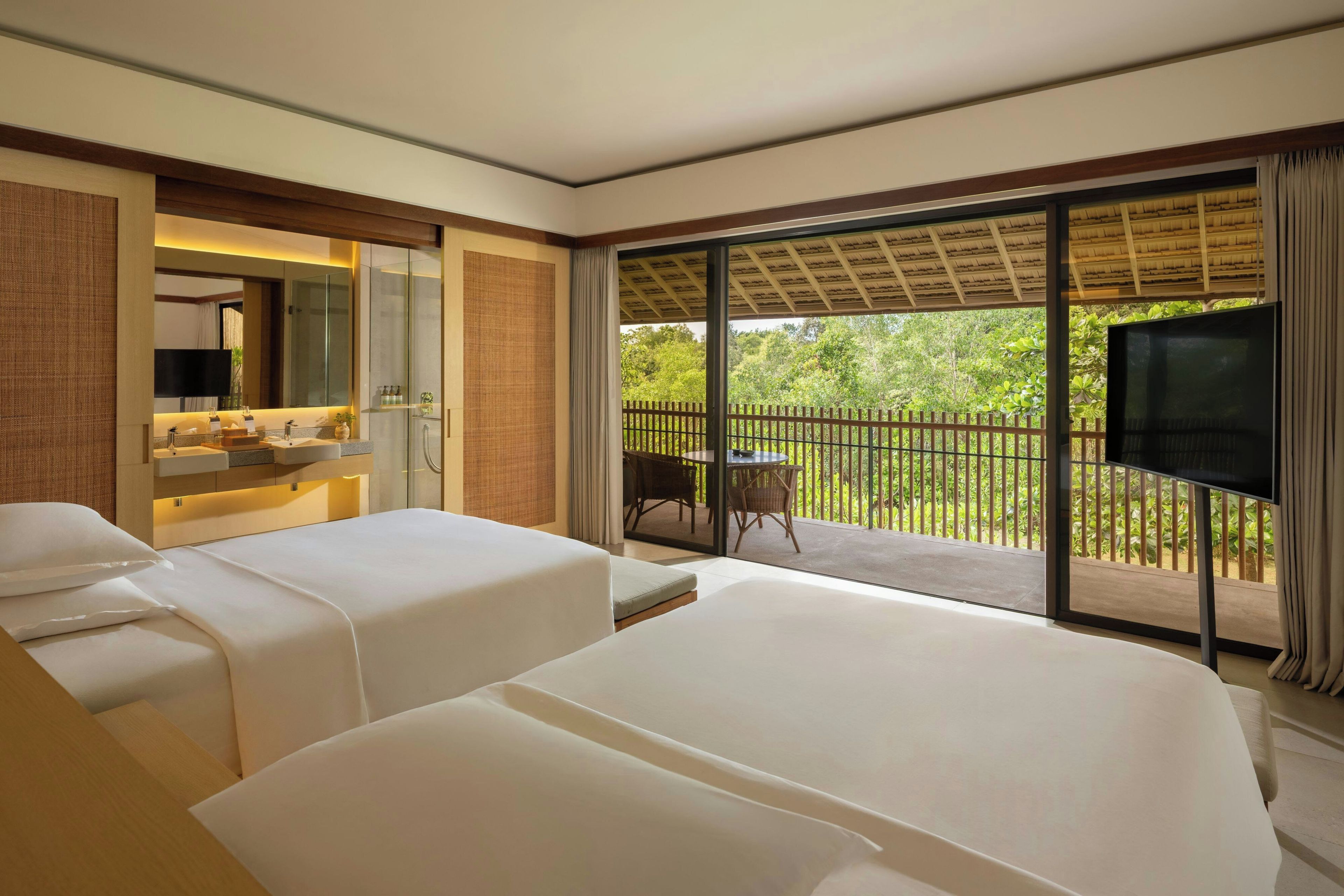 Une chambre d’hôtel avec deux lits, une salle de bain, un balcon avec un téléviseur et une vue sur la verdure.