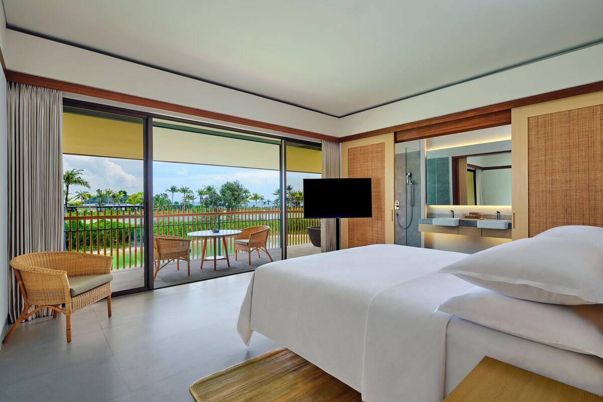 A hotel room with a bed, a TV, a bathroom with a mirror, and a balcony with a table and chairs.