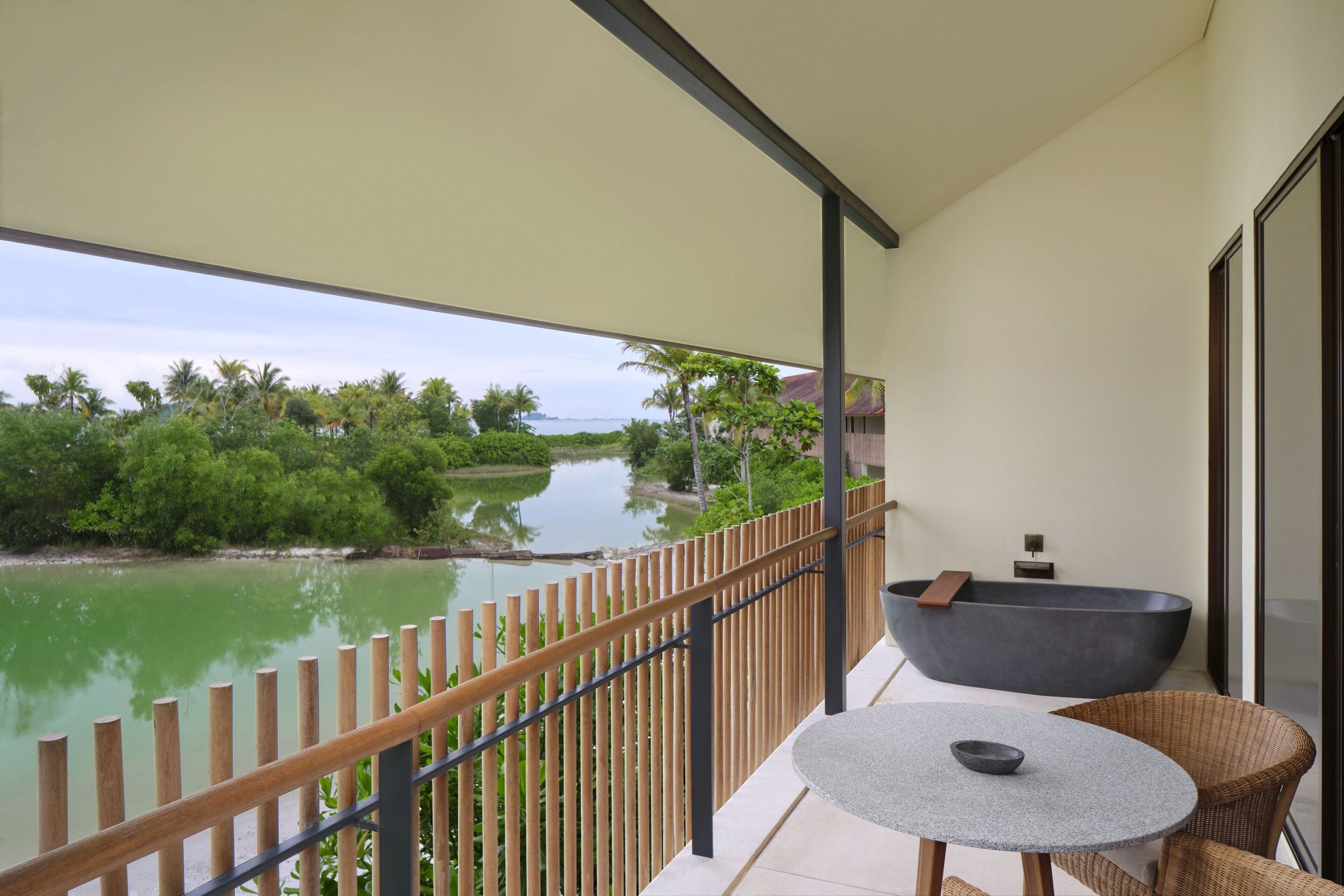 A balcony with a view of a lake, a large bathtub, and wicker furniture.