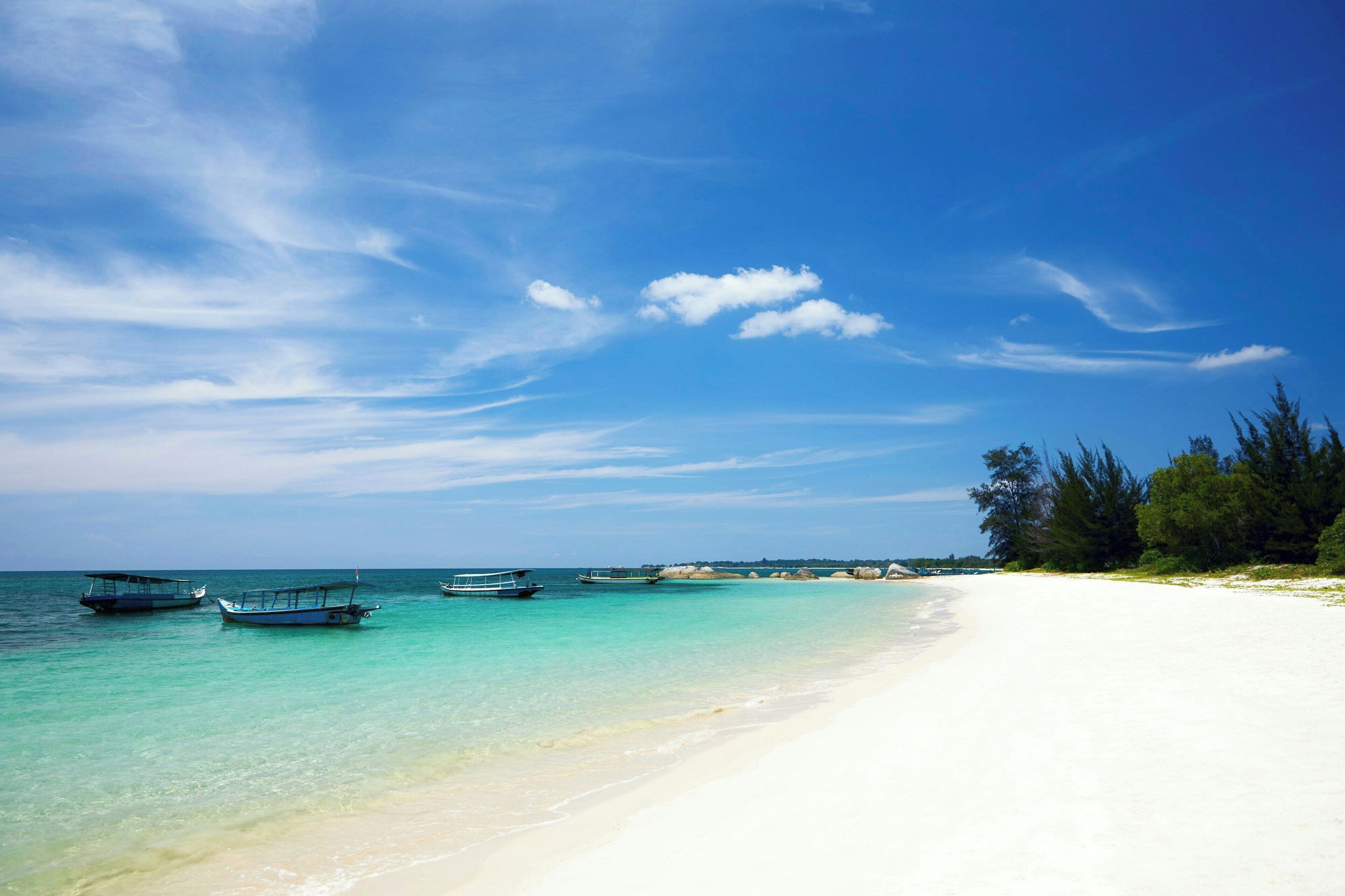 A beach with clear turquoise water, boats, and a white sandy shore.
