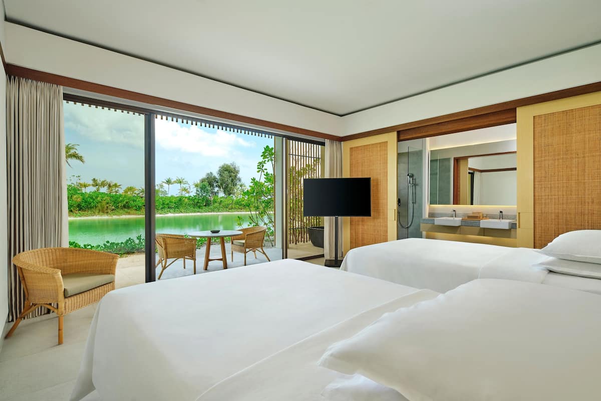 A hotel room with two beds, a TV, a bathroom with a mirror, and a view of a pool and greenery.