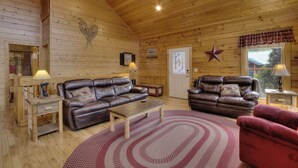 A wooden cabin interior with two leather sofas, a wooden coffee table, and a red rug. - Serenity Now #370 (Pigeon Forge)