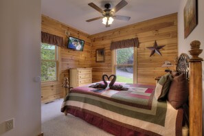 A bedroom with a wooden interior, a bed with a quilt, a ceiling fan, a television, and a star decoration on the wall. - Serenity Now #370 (Pigeon Forge)