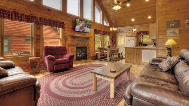 A spacious living room with a fireplace, leather sofas, a television, and a dining area with wooden furniture. - Serenity Now #370 (Pigeon Forge)