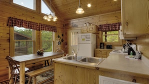 A wooden cabin kitchen with a wooden table, bench, and a refrigerator. - Serenity Now #370 (Pigeon Forge)
