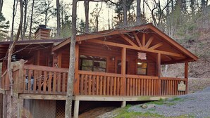A wooden cabin with a porch, a chimney, and a sign indicating it's a rental property. - Secret Hideaway #195 by Aunt Bug's Cabin Rentals (Sevierville)