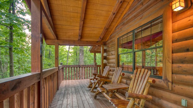 A wooden deck with log walls, outdoor seating, and a view of the forest. - Secret Hideaway #195 by Aunt Bug's Cabin Rentals (Sevierville)