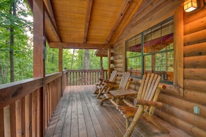 A wooden deck with log walls, outdoor seating, and a view of the forest.