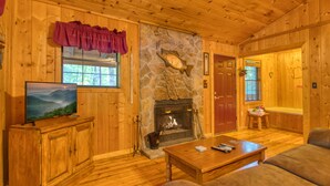 A wooden cabin interior with a stone fireplace, wooden furniture, and a television on a cabinet. - Secret Hideaway #195 by Aunt Bug's Cabin Rentals (Sevierville)