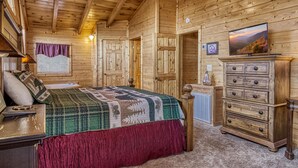 Une chambre dans un chalet en rondins, avec un lit, une commode et un téléviseur diffusant un paysage pittoresque.
