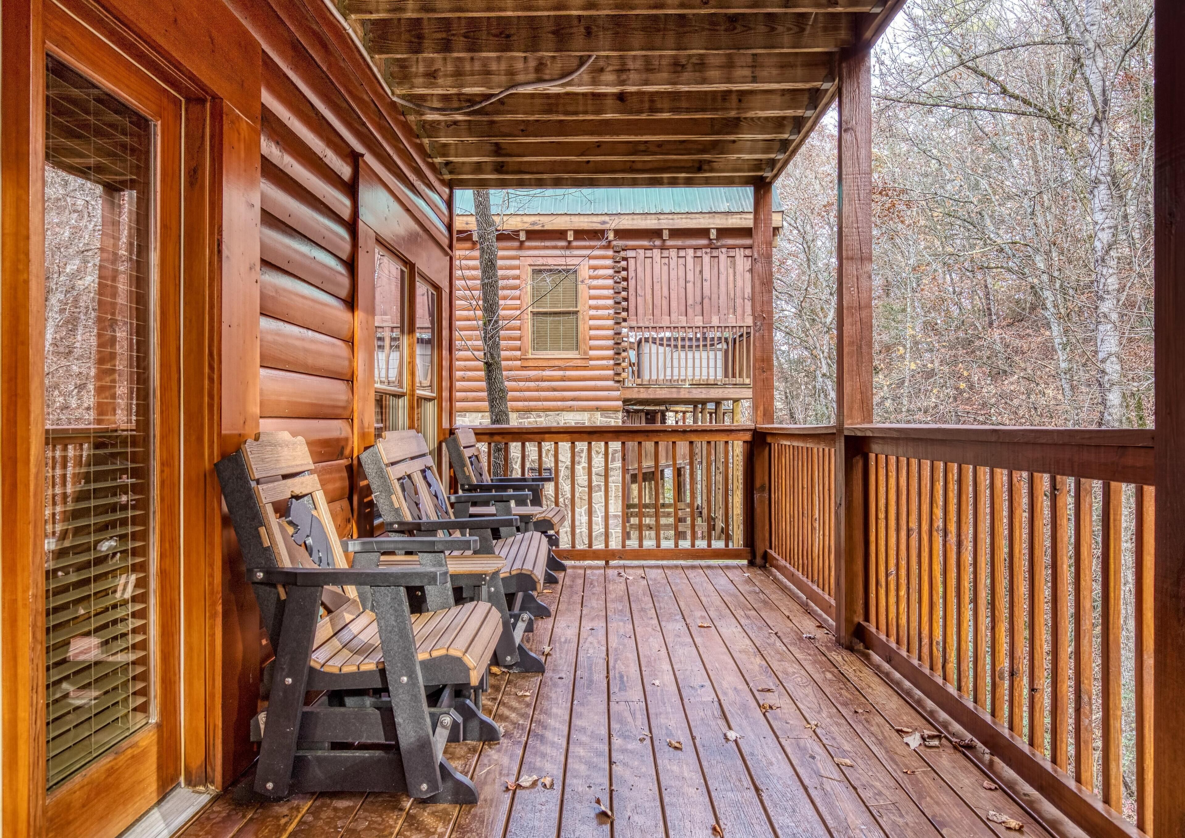 A wooden cabin with a porch seating area and a view of a forest.