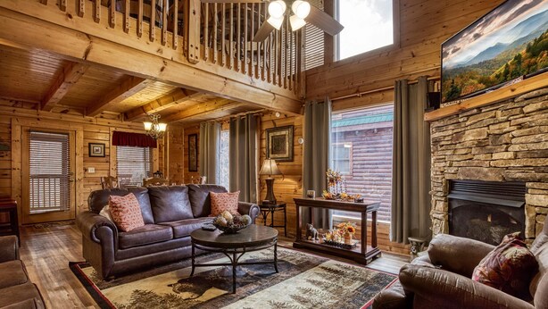 L’intérieur d’une cabane en rondins, avec une cheminée, un canapé, une table basse et un lustre.