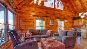A log cabin interior with a living room featuring leather sofas, a wooden floor, and a kitchen area with wooden cabinets. - Poolside Retreat #221 by Aunt Bug's Cabin Rentals (Sevierville)