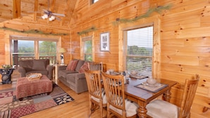 A cozy cabin interior with a wooden dining table, two sofas, and a fireplace. - Poolside Retreat #221 by Aunt Bug's Cabin Rentals (Sevierville)