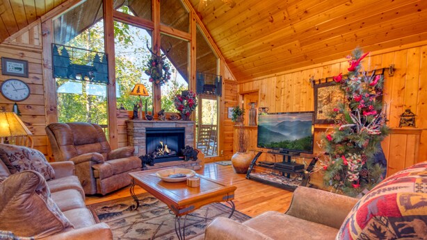 Un acogedor interior de cabaña de madera con chimenea, asientos cómodos, televisión y decoración festiva.