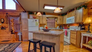 Cocina de estilo cabaña con isla central, taburetes de bar y un refrigerador.