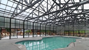 Una piscina interior con techo de cristal, rodeada de sillones de descanso.
