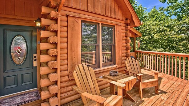 Una cabaña de madera con un porche, dos sillas Adirondack y una pequeña mesa.