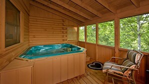 Una cabaña de madera con jacuzzi, una ventana y una silla.