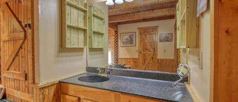 A wooden bathroom with a large mirror, a sink, and wooden cabinets.