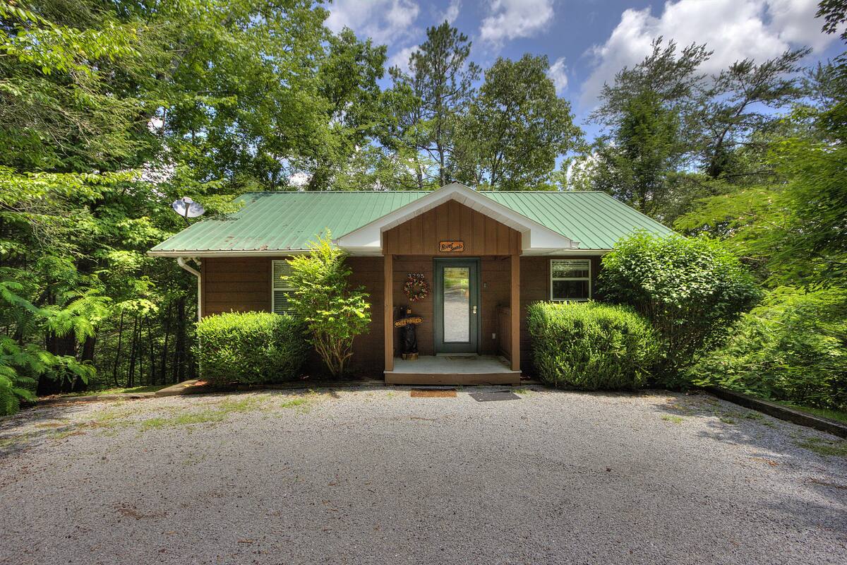 A lodge with a green metal roof, a wooden front porch, and a gravel driveway.