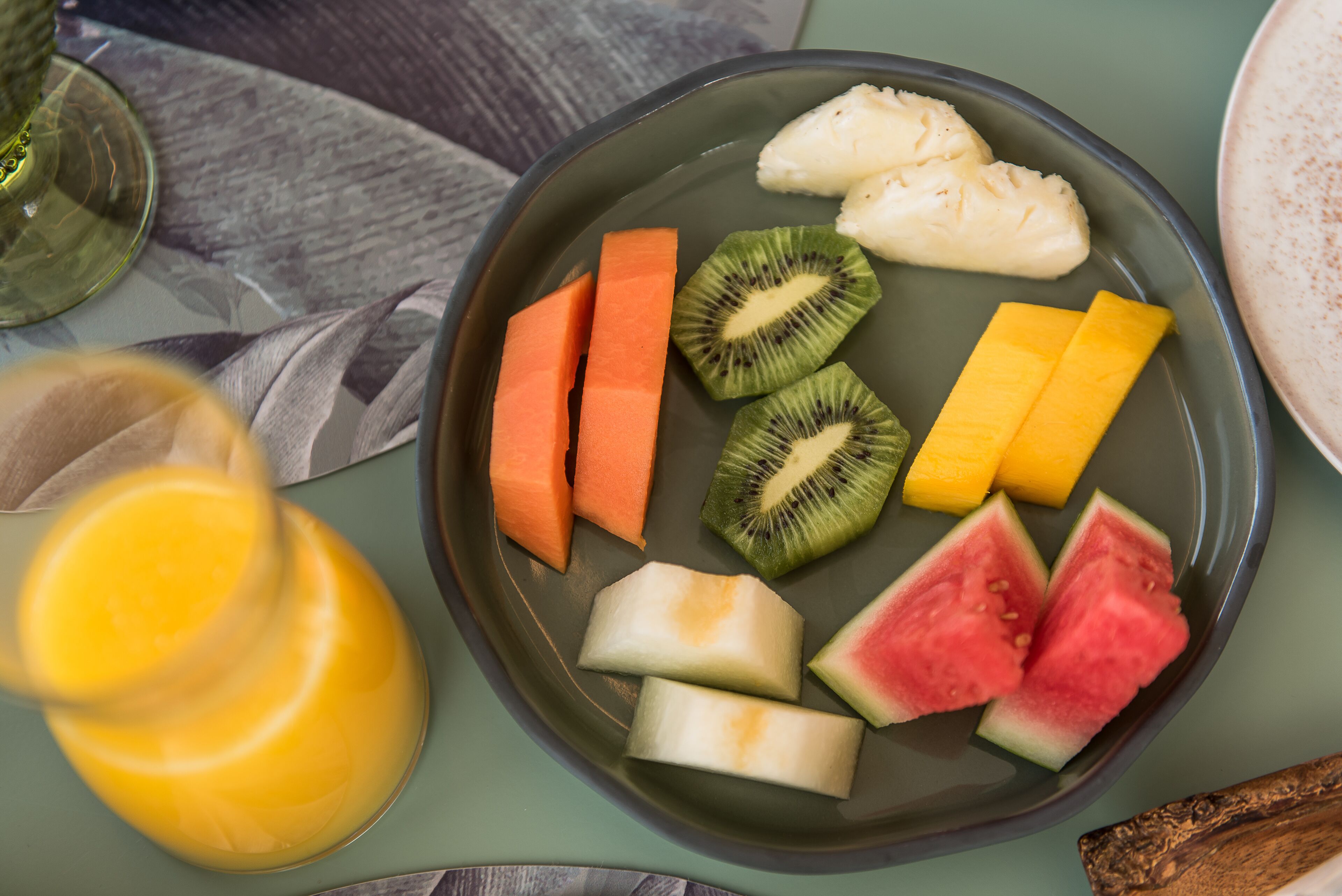 A plate with sliced fruits and a glass of orange juice.