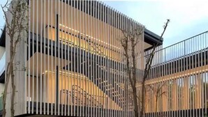Un edificio moderno con una fachada vertical de madera distintiva, una base de piedra y una escalera que conduce a un nivel superior.