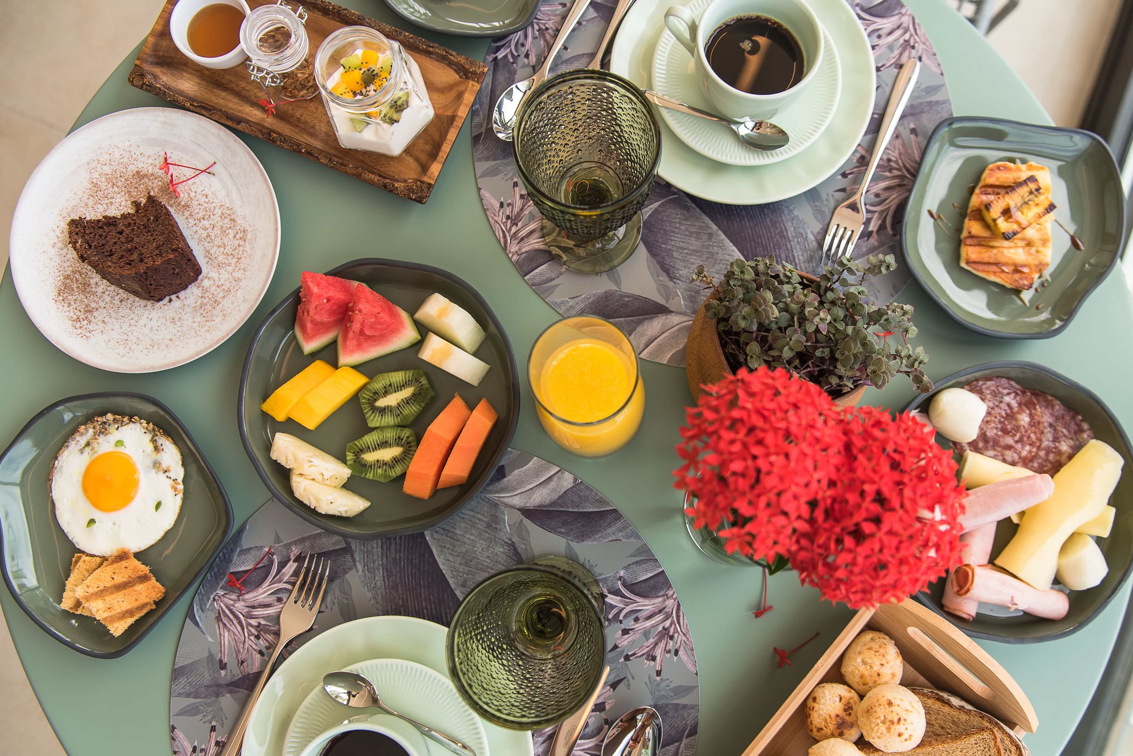 A breakfast setting with various dishes, including eggs, fruits, and pastries, arranged on a table with a floral tablecloth.