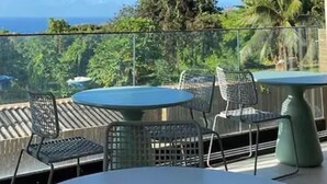 Un balcón con mesa y sillas, con vistas a un paisaje con mar y vegetación.