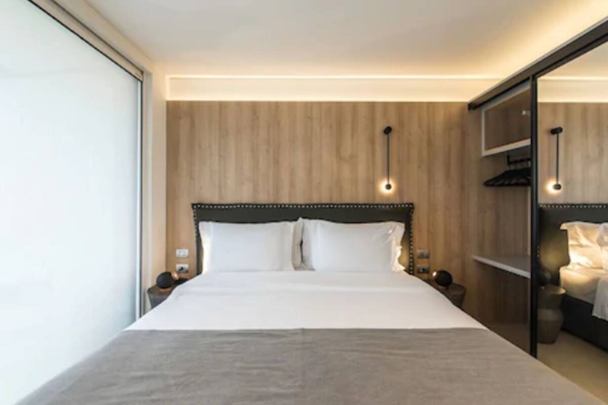 A modern hotel room with a large bed, wooden panel walls, and a built-in wardrobe.
