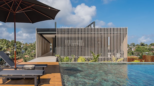 Un área de piscina moderna con cubierta de madera, sillas de descanso y una sombrilla grande.