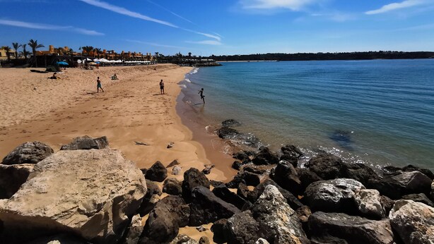 Ein Strand mit blauem Himmel, felsigem Ufer und Menschen, die die Sonne genießen.